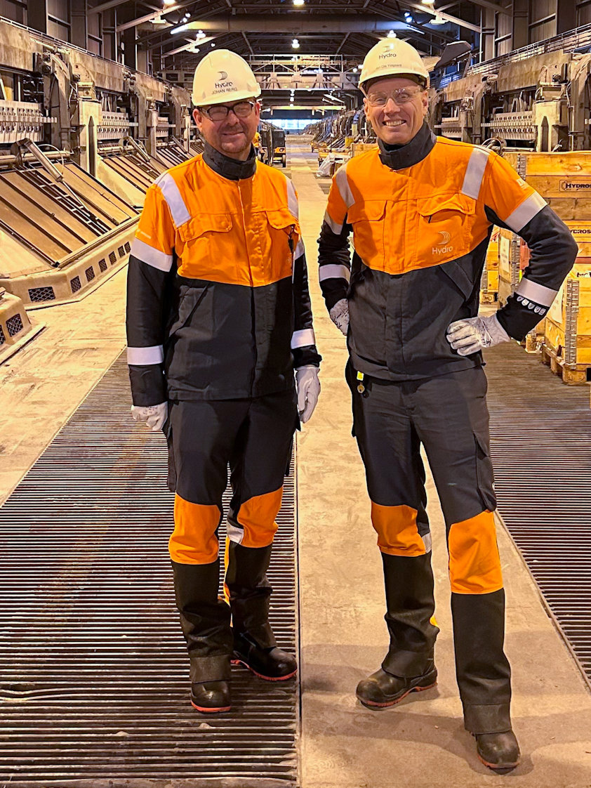 a couple of men in safety gear standing on a factory floor