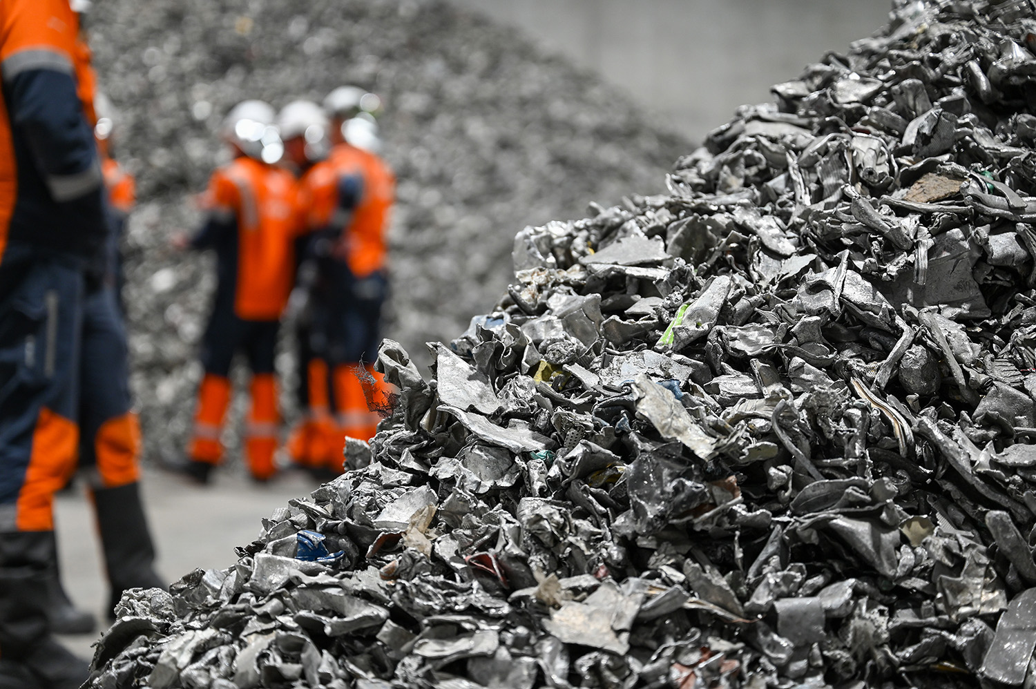 a group of workers in orange vests standing next to a pile of aluminium scrap