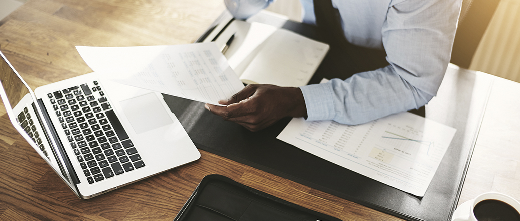 man holding a sheet of paper at desk with laptop